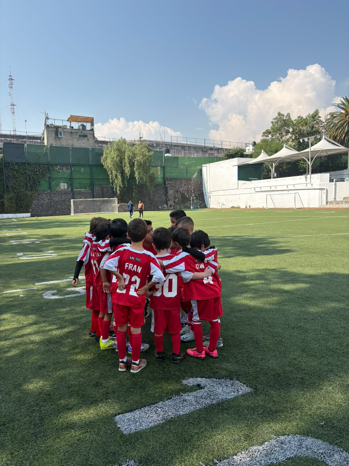 Niños del Curso de Verano Little Kickers en círculo de equipo en el Colegio Merici